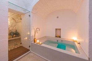 Une salle de bain moderne avec une baignoire sur pieds, une petite étagère avec des bougies et un mur en pierre.