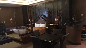 A modern hotel room with a large bed, a sitting area with a sofa and chairs, a dining table, and a decorative wall with intricate patterns. - Amani SPA Boutique Motel (Toufen)