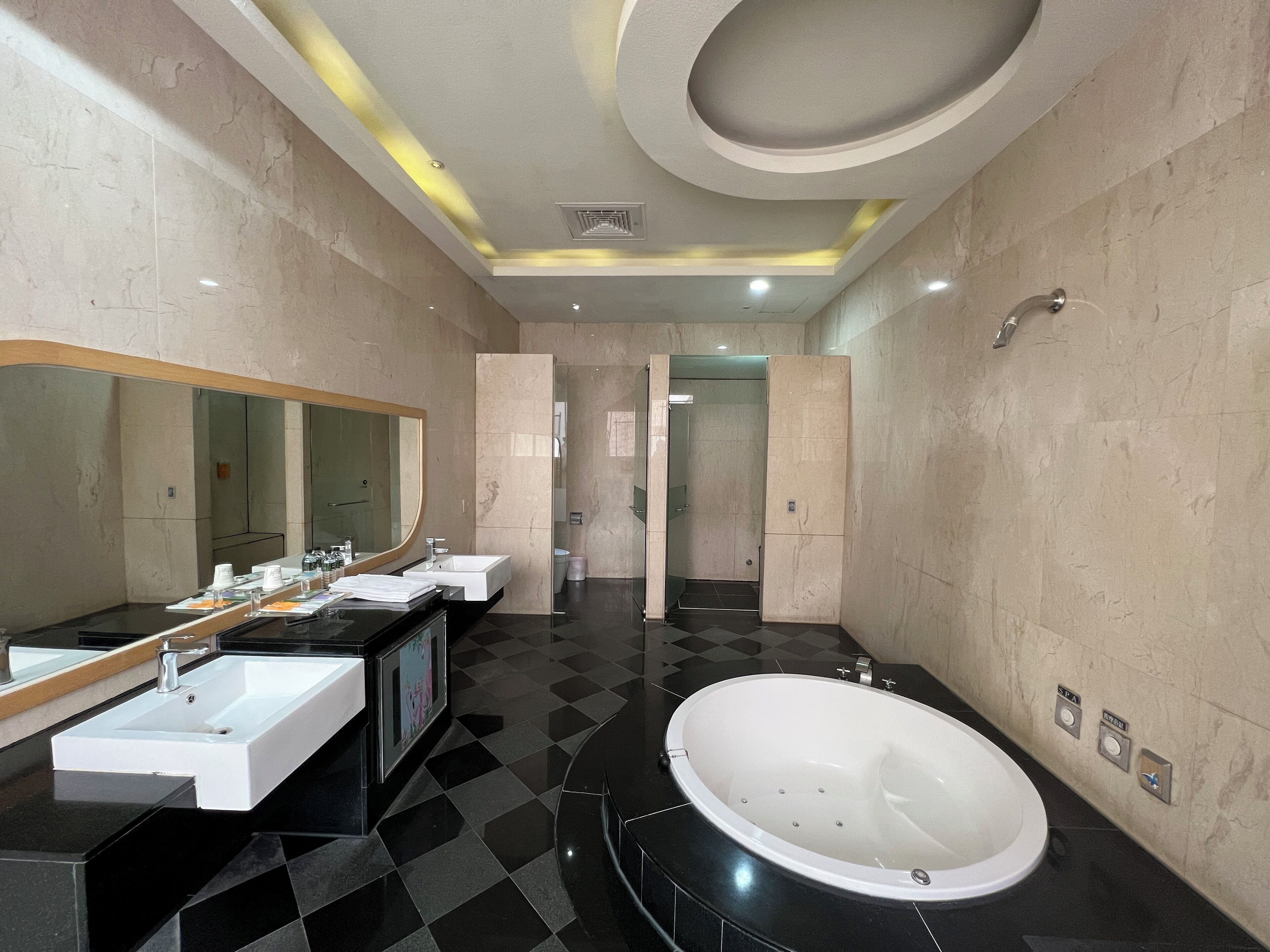 A modern bathroom with a large mirror, two sinks, a bathtub, and a shower area.
