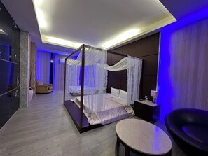 Un dormitorio moderno con cama con dosel, una mesa redonda y una zona de estar con sofá y sillón.