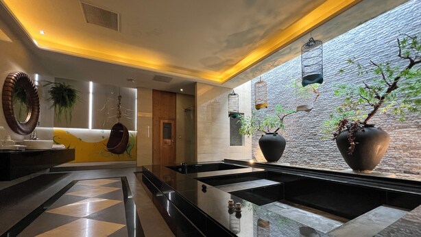 A modern lobby with a checkered floor, a reception desk, and a large window with a view of a brick wall and hanging birdcages. - Amani SPA Boutique Motel (Toufen)