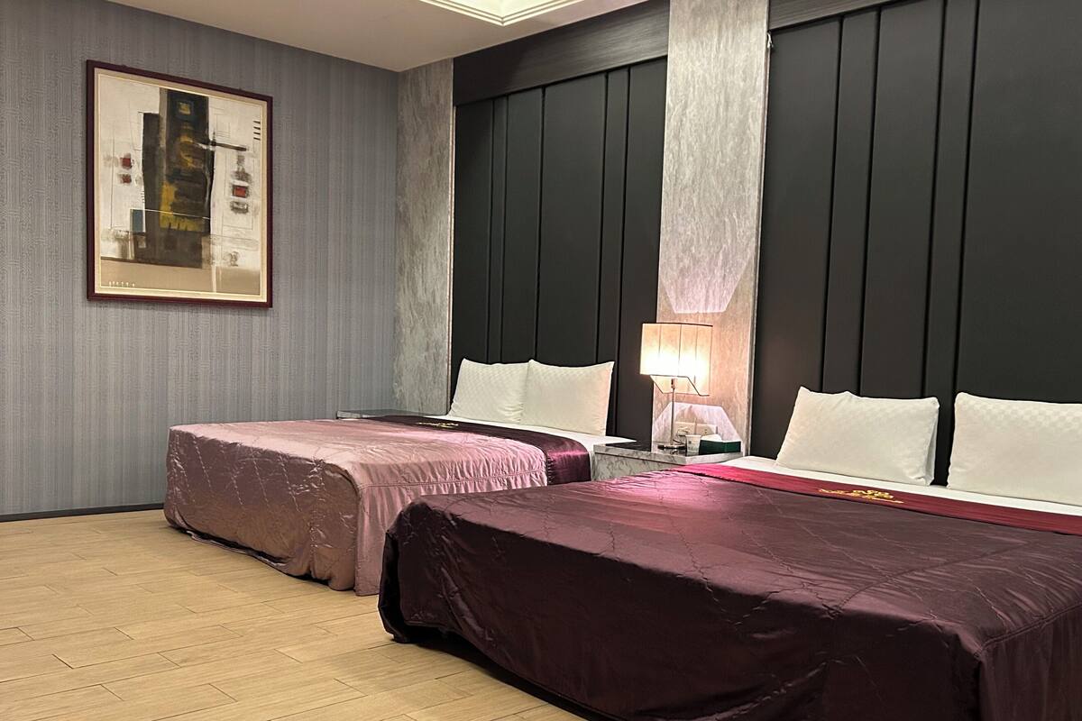 Ein Hotelzimmer mit zwei Betten, einem Nachttisch, einer Lampe und einem gerahmten Bild an der Wand.
