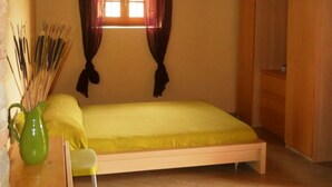 A small room with a bed, a chair, a wooden wardrobe, and a window with curtains. - Libeccio studio apartment with panoramic view of the hills (Toscana)