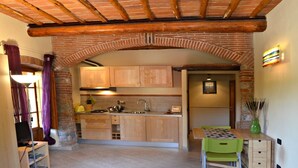 A compact kitchen with wooden cabinets, a sink, and a dining area with a green table and chairs. - Libeccio studio apartment with panoramic view of the hills (Toscana)