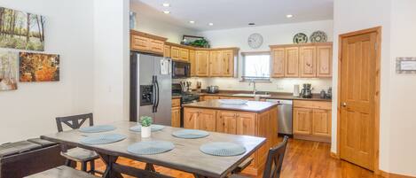 A modern kitchen with wooden cabinets, a central island, and a dining area with a wooden table and benches.