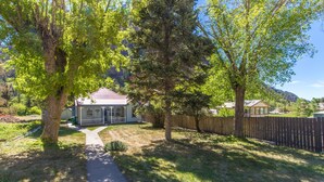 A residential property with a house, a wooden fence, and a pathway leading to the house. - Cozy Downtown Pet Friendly Home with Fiber Internet! Fenced Outdoor Area! (Ouray)