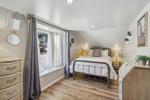 Une chambre à coucher comprenant un lit, des tables de chevet, une commode, une fenêtre avec des rideaux et une vue sur l’extérieur.