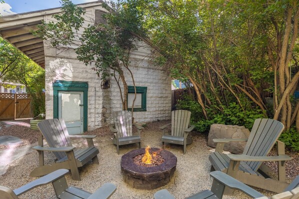 Un espace patio avec des fauteuils Adirondack, un foyer et un bâtiment blanc aux bordures vertes.