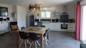 A modern kitchen with white cabinets, a wooden dining table, and a red curtain. - BETWEEN LAKES AND MOUNTAINS - DETACHED HOUSE AIR-CONDITIONED 3-BEDROOM WITH ENCLOSED GROUNDS (Barésia-sur-l'Ain)
