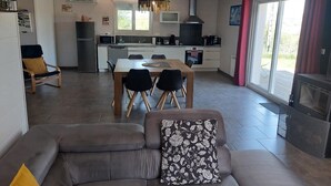 A modern living room with a sofa, a dining table with chairs, a kitchen area with a stove, and a fireplace. - BETWEEN LAKES AND MOUNTAINS - DETACHED HOUSE AIR-CONDITIONED 3-BEDROOM WITH ENCLOSED GROUNDS (Barésia-sur-l'Ain)