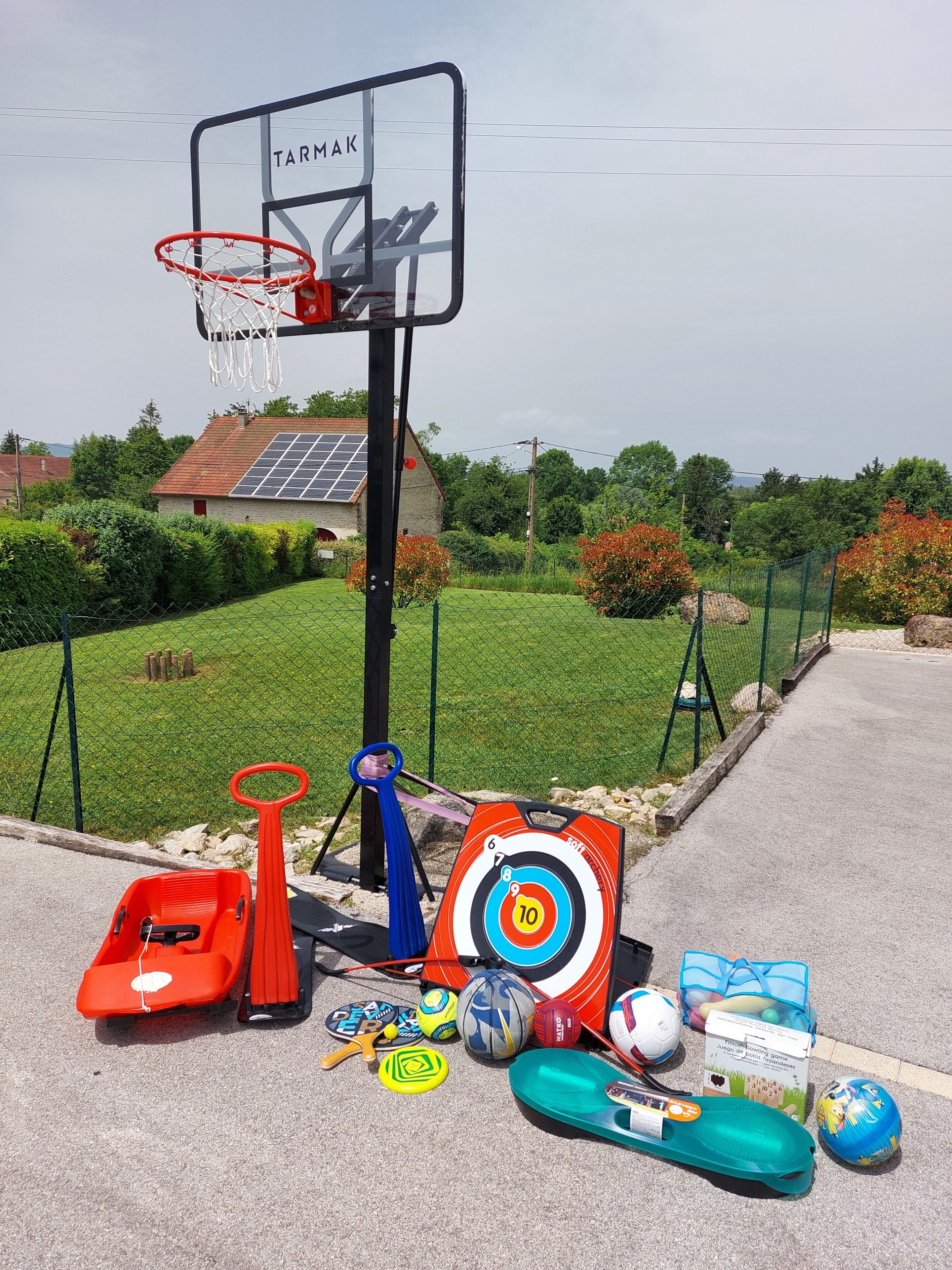 Un panier de basket avec un panneau cible, une trottinette et divers équipements sportifs sur une surface pavée.