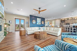 A spacious living room with a large white sofa, a wooden coffee table, and striped blue and white armchairs.