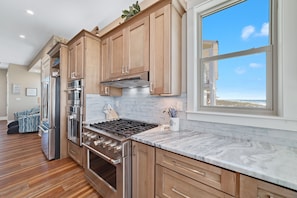 A modern kitchen with wooden cabinets, stainless steel appliances, and a large window offering a view.