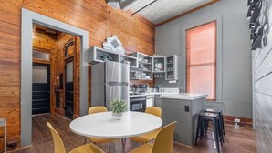 A modern kitchen with wooden walls, a central island, and yellow chairs around a white table.