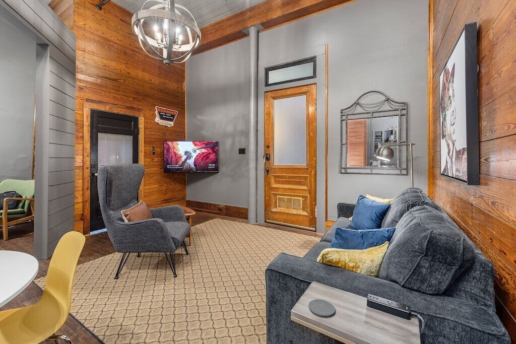 Ein gemütliches Wohnzimmer mit einem grauen Sofa, einem gelben Sessel, einer Holzvertäfelung, einem Fernseher und einer Tür.