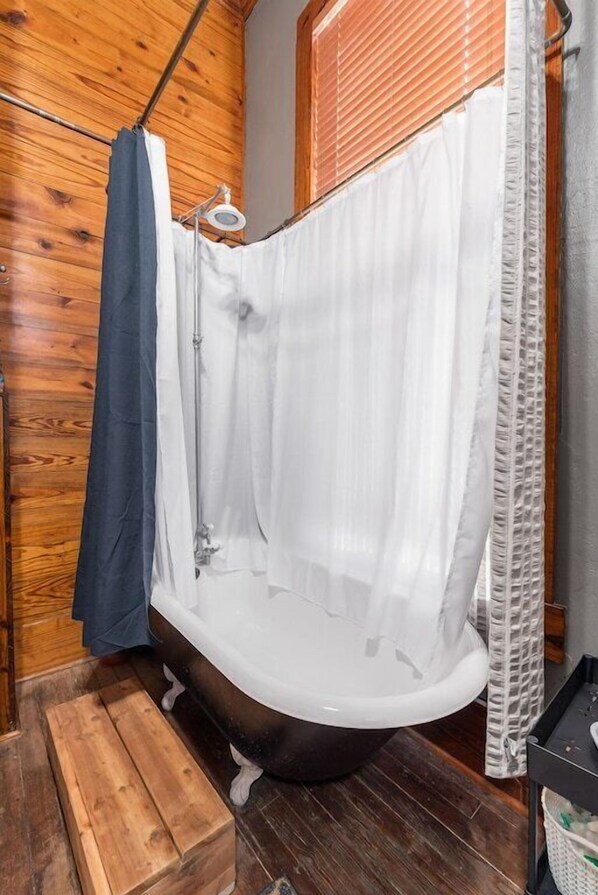A bathroom with a wooden floor, a white bathtub, and a shower curtain.