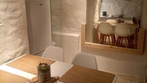 A dining area with a white table set with woven placemats and white chairs. A glass cabinet with a plant is on the table. - "LE Temps Suspendu"studio de Charme3,filet de Détente Suspendu (Malaucène)