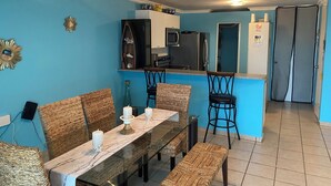 A dining area with a glass table, wicker chairs, and candles. There is a kitchen area with a microwave and refrigerator. - PR-PARADISE, Serenity-3-BEDROOM-2 BathRM- APT -PARKING, POOL-WiFI-close to BEACH (Rio Grande)