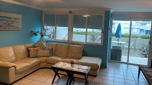 A living room with a beige sectional sofa, a coffee table with a lace table runner, and a painting on the wall. - PR-PARADISE, Serenity-3-BEDROOM-2 BathRM- APT -PARKING, POOL-WiFI-close to BEACH (Rio Grande)