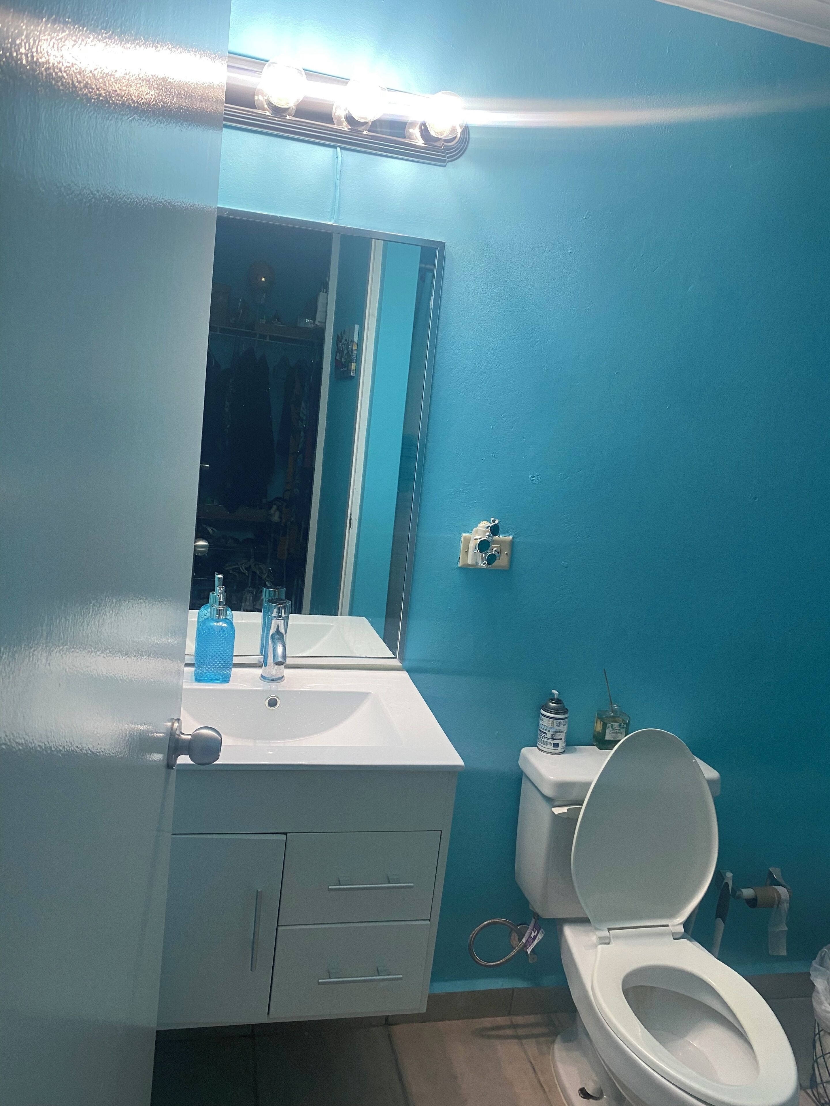 Een badkamer met een witte wastafel, spiegel en toilet. Er staan toiletartikelen op de wastafel en een handdoekhouder boven het toilet.