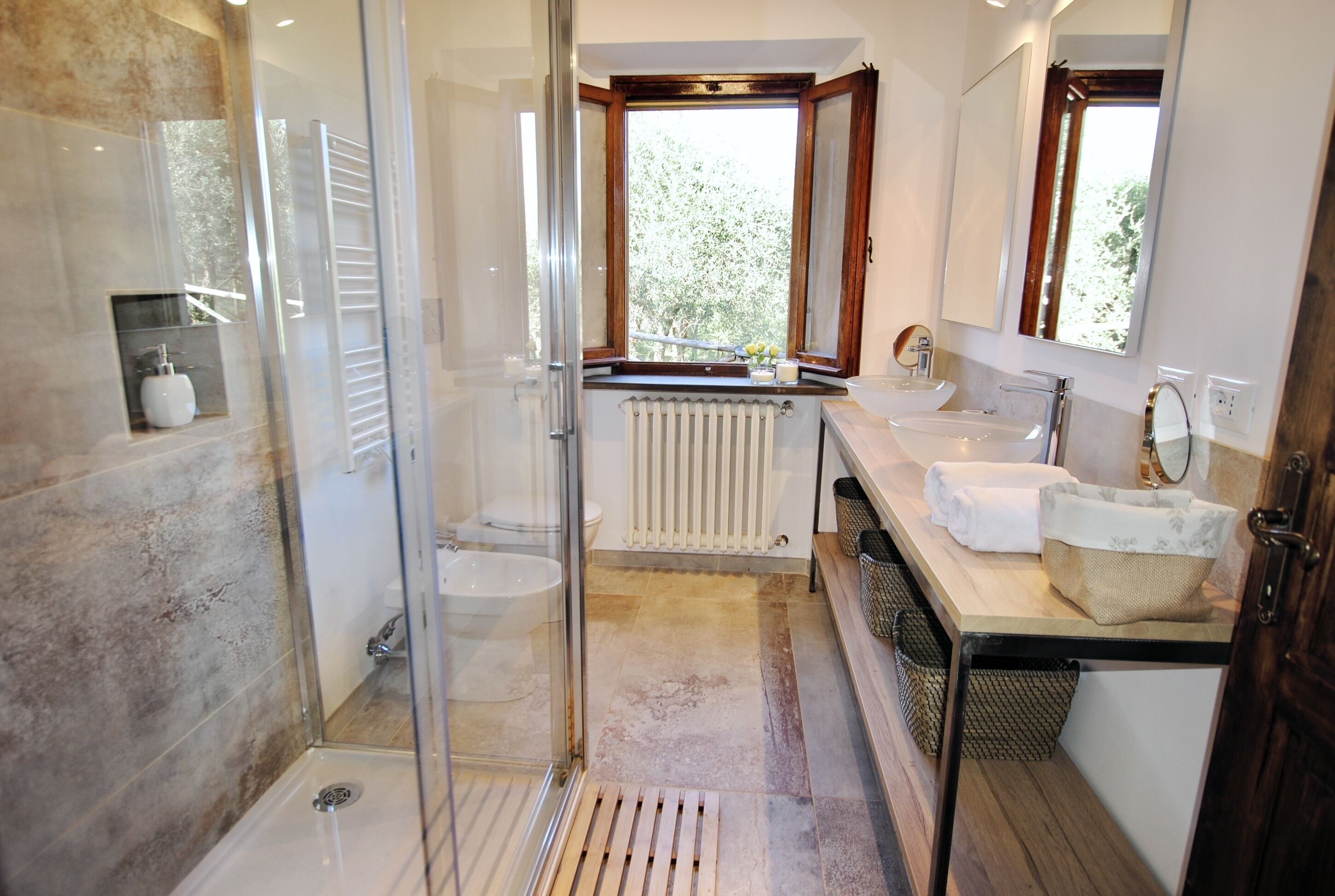 A modern bathroom with a glass shower enclosure, dual sinks, and a window providing natural light.