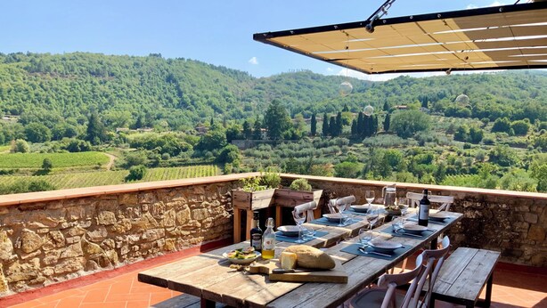 An outdoor dining area with a stone wall and a view of vineyards. - Chianti Tuscany: a villa with a view (Lucolena)