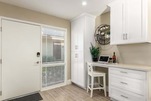A compact kitchen with white cabinetry, a dining area with a white chair, and a small table with a laptop and wine bottle.