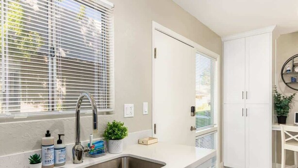 A modern kitchen with a double sink, white cabinets, and a window with blinds. - Fashion Square Retreat | Walk Everywhere + 4 Pools (Scottsdale)
