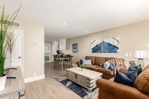 A living room with a brown sofa, a wooden coffee table, and a dining area with a table and chairs.