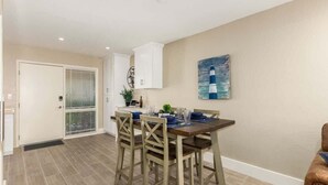 A dining area with a wooden table and chairs, a painting on the wall, and a door with a window. - Fashion Square Retreat | Walk Everywhere + 4 Pools (Scottsdale)
