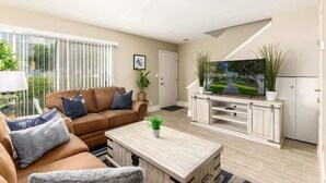 A modern living room with a brown leather sofa, a coffee table, and a TV on a wooden stand. - Fashion Square Retreat | Walk Everywhere + 4 Pools (Scottsdale)