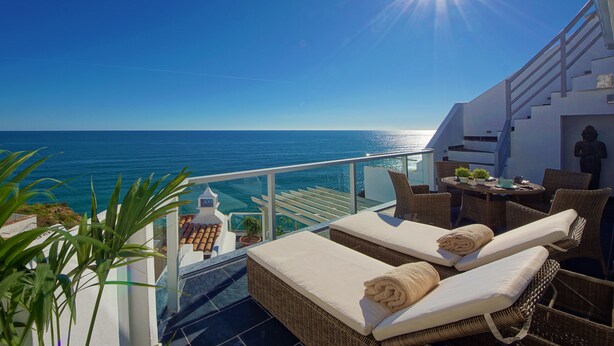 Un balcone con mobili in vimini, un tavolo con piante e vista sul mare.