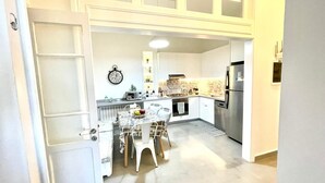 A modern kitchen with white cabinets, a stainless steel refrigerator, and a dining area with a table and chairs. - Broummana House (Broumana)