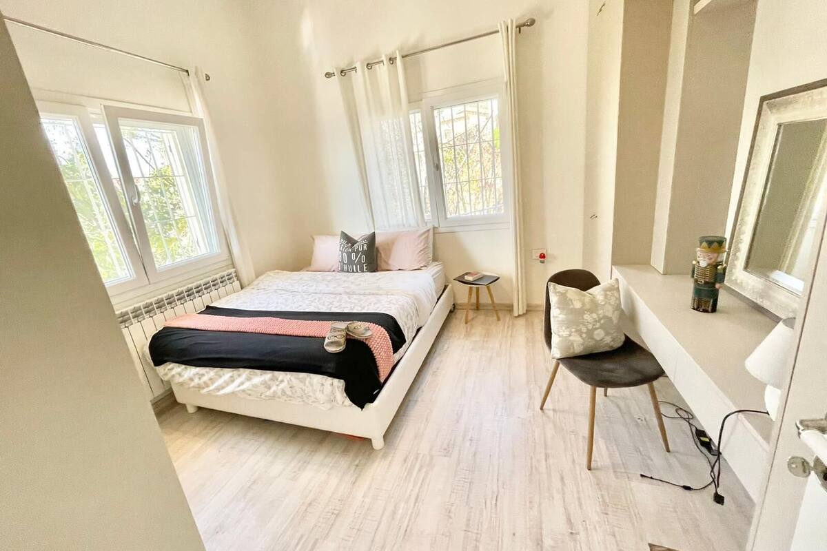 Quarto com cama, mesa de cabeceira pequena, cadeira e janela com cortinas.