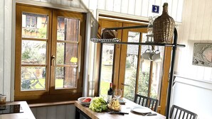 A kitchen with a wooden table, chairs, a hanging light fixture, and a window with a view of the outside. - LE CAFÉ SALON bei der Weinstraße 20Min von Straßburg. (Rangen)