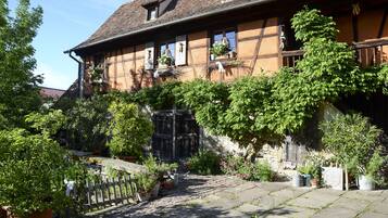 A traditional half-timbered house with a stone courtyard, potted plants, and a wooden fence.