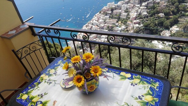 A balcony with a table featuring a floral tablecloth and a vase with sunflowers. - CASA INCANTO, beautiful house with stunning views and parking space (Positano)