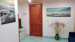 A room with a wooden door, a flat-screen TV on a white cabinet, a painting on the wall, and a vase with dried plants. - CASA INCANTO, beautiful house with stunning views and parking space (Positano)