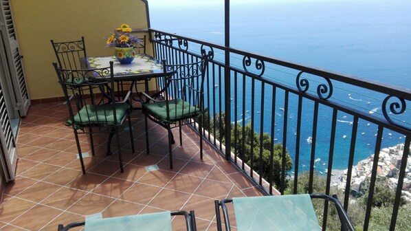 Un balcon avec une table et des chaises, un vase de fleurs et une vue sur la mer.