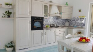 A kitchen with white cabinets, a black oven, and a tiled backsplash. There is a dining table with a fruit bowl on it. - CASA INCANTO, beautiful house with stunning views and parking space (Positano)