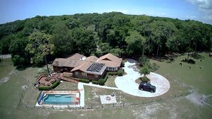 A house with a swimming pool, surrounded by a fenced yard and a forested hill. - Former Hunting Lodge on 24 Acres with Lake with heated pool (Spring Hill)