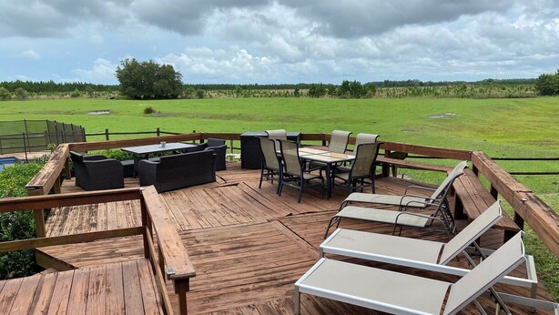 A wooden deck with outdoor furniture, including chairs and a table, overlooking a grassy field. - Former Hunting Lodge on 24 Acres with Lake with heated pool (Spring Hill)