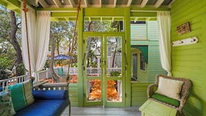 A porch with a swing, a cushioned bench, and a wicker chair with a cushion. - Amazing Porches, Steps From Seaside, FL Beach! One Story + 2 Adult Bikes! (Santa Rosa Beach)