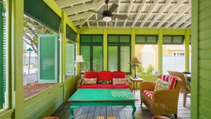 A covered porch with a green and white color scheme, a red sofa with cushions, a green table with a chessboard, wicker chairs, and a ceiling fan. - Amazing Porches, Steps From Seaside, FL Beach! One Story + 2 Adult Bikes! (Santa Rosa Beach)