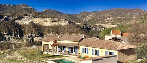 A two-story house with a swimming pool, surrounded by a hilly landscape.
