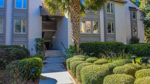 A two-story building with a balcony, a palm tree, and neatly trimmed bushes. - 3 Min Walk to Beach & Marina-Free Bikes/Pool/Tennis (Hilton Head Island)