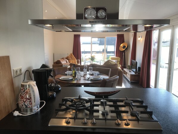A modern kitchen with a gas stove, a kettle, and a dining area with a sofa and table set for two.