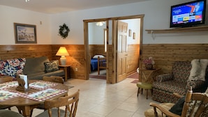 Un salon chaleureux avec un plancher en bois, une table à manger avec des chaises, un canapé et un téléviseur fixé au mur.