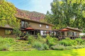 Une maison à deux étages dotée d’un balcon, d’un jardin avec différentes espèces de plantes et offrant une vue sur un paysage montagneux.