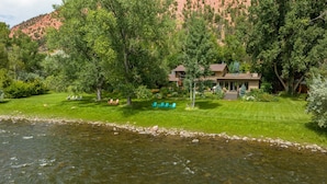 A house with a well-maintained lawn, outdoor seating, and a river in the foreground. - River Frontage! Family Friendly Mtn Retreat (Glenwood Springs)